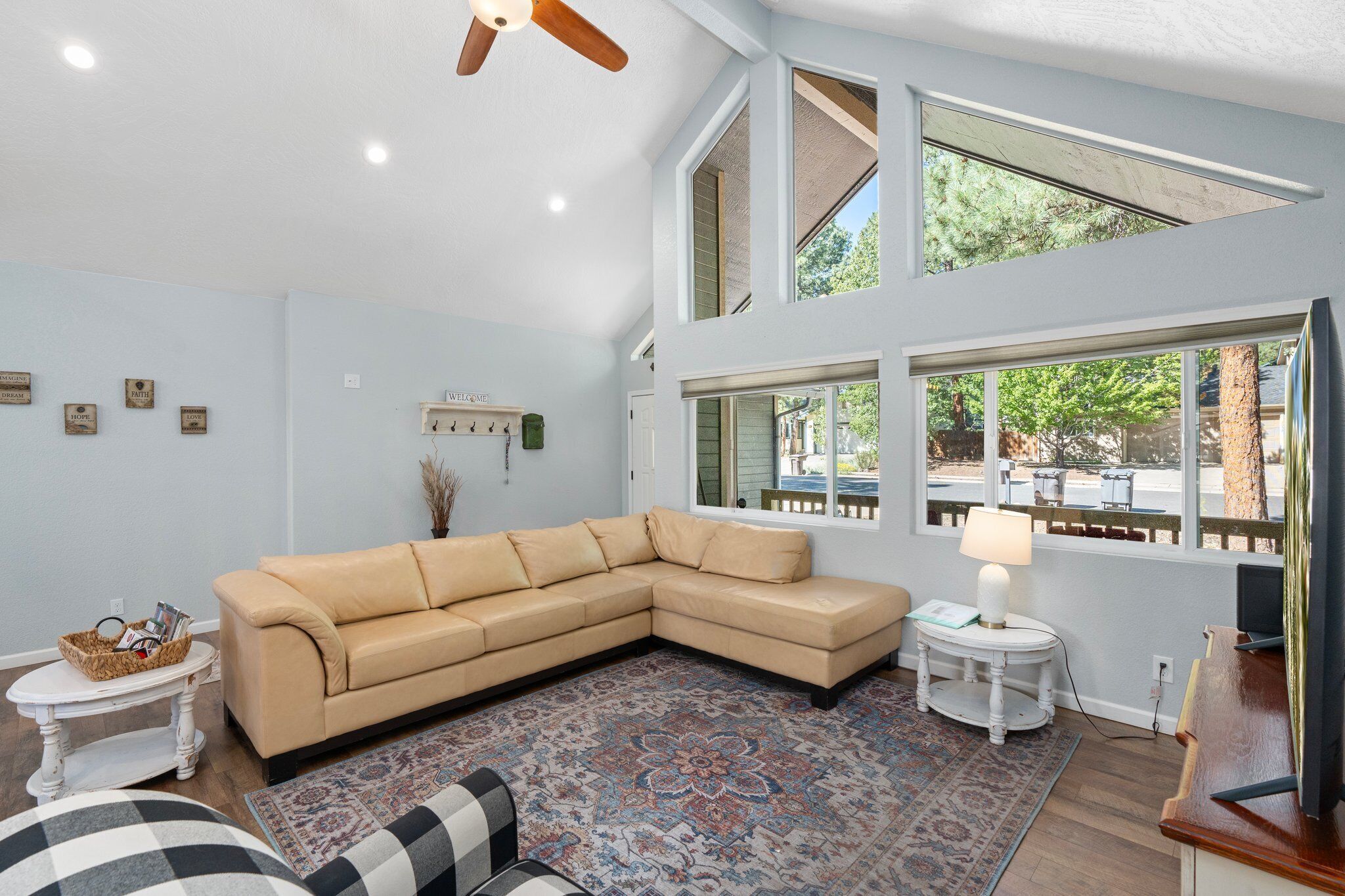 A living room with a beige sectional sofa, a patterned rug, a small round table with a lamp, and a television on a wooden stand.