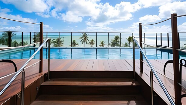 A wooden deck leading to a pool with a clear view of the ocean and palm trees. - Infinity At The Sea (João Pessoa)