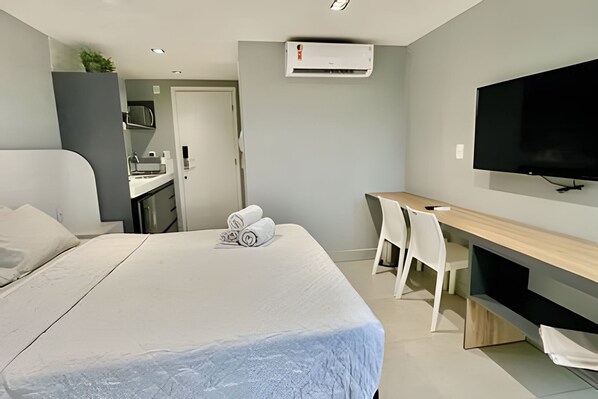 A modern hotel room with a bed, a desk, a chair, a television, and an air conditioning unit. - Infinity At The Sea (João Pessoa)