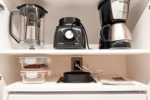 A kitchen with a coffee maker, a blender, and a kettle on the shelf, and a stove with pots and pans below. - Infinity At The Sea (João Pessoa)