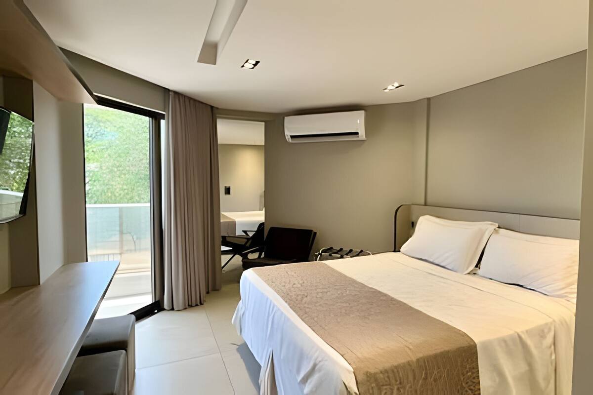 A modern hotel room with a bed, a desk, a chair, and a balcony with curtains.