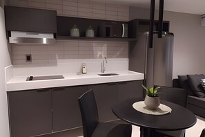 A modern kitchen with a white countertop, stainless steel appliances, and a round dining table with a potted plant. - Infinity At The Sea (João Pessoa)