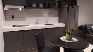A modern kitchen with a white countertop, stainless steel appliances, and a round dining table with a potted plant. - Infinity At The Sea (João Pessoa)