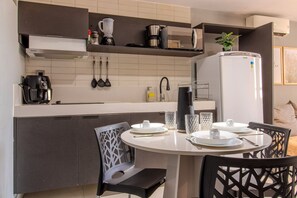 A compact kitchen with modern appliances, a dining table with chairs, and a refrigerator. - Infinity At The Sea (João Pessoa)