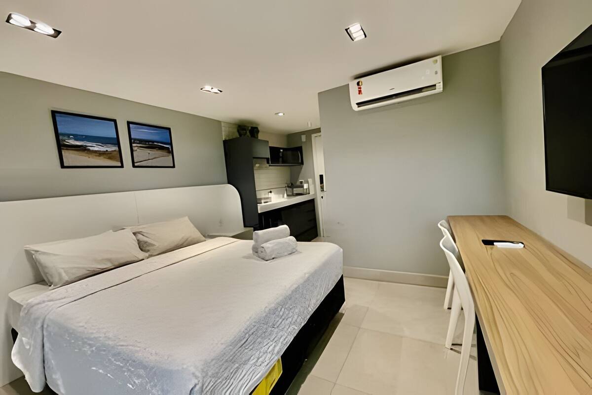 A modern hotel room with a bed, a desk, a TV, and an air conditioning unit.