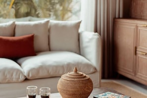 A living room with a sofa, a coffee table with a decorative vase, and a cabinet. - Namia River Retreat - Wellness Inclusive Resort (Hoi An)