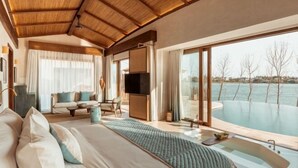 A spacious bedroom with a large bed, a sofa, a television, and a view of a swimming pool. - Namia River Retreat - Wellness Inclusive Resort (Hoi An)
