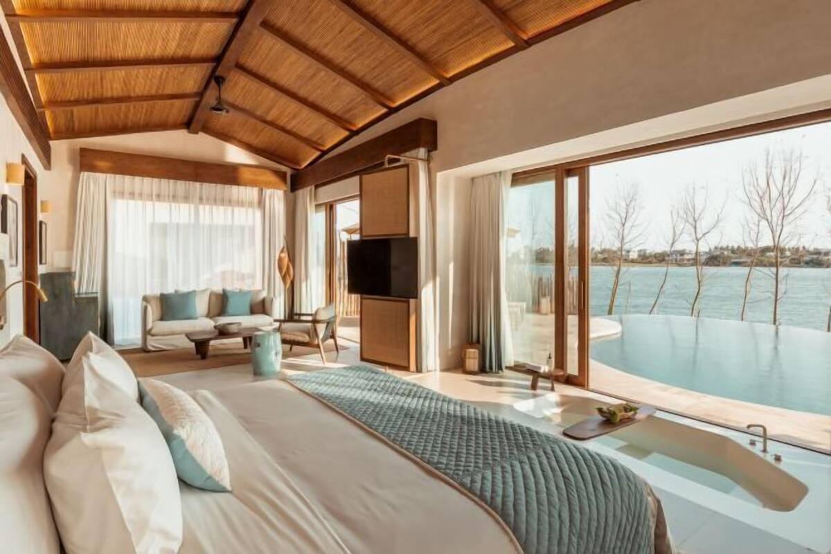 A spacious bedroom with a large bed, a sofa, a television, and a view of a swimming pool.