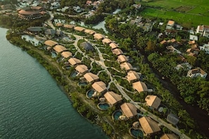 An aerial view of a resort with circular buildings, a water body, and surrounding greenery. - Namia River Retreat - Wellness Inclusive Resort (Hoi An)