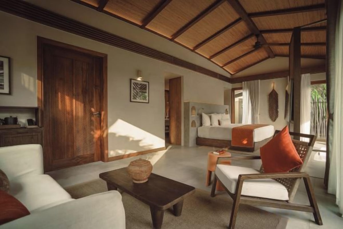 A spacious room with a high ceiling, a bed, a seating area with a table, and a door leading to another room.