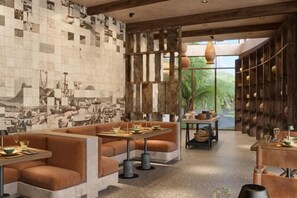 A restaurant with high tables and booths, a patterned wall, and a large window with a view of greenery. - Namia River Retreat - Wellness Inclusive Resort (Hoi An)