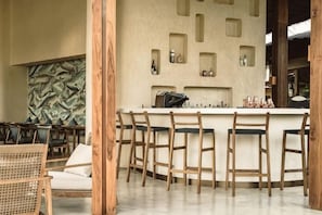 A bar area with wooden chairs and a white bar counter, surrounded by wooden pillars. - Namia River Retreat - Wellness Inclusive Resort (Hoi An)
