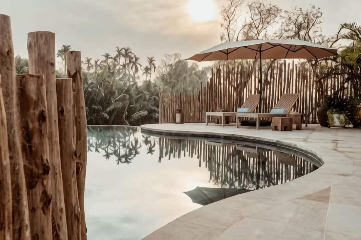 A pool with wooden fencing, lounge chairs, and an umbrella.