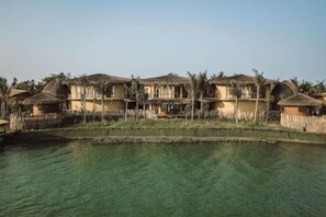 A row of thatched-roof cottages by a calm water body, likely a resort setting. - Namia River Retreat - Wellness Inclusive Resort (Hoi An)