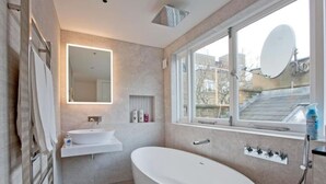 Ein modernes Badezimmer mit einer freistehenden Badewanne, einem Waschtisch mit Spiegel und einem Fenster mit Aussicht.