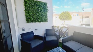 A balcony with wicker furniture, a green wall, and a view of buildings and a tree. - Playitas Salema Apartment (Las Playitas)