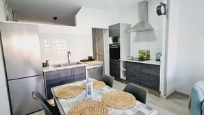 A modern kitchen with a refrigerator, stove, and sink. There is a dining table with placemats and chairs. - Playitas Salema Apartment (Las Playitas)