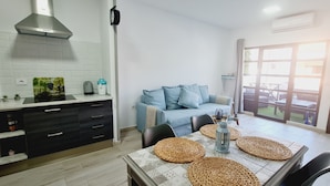 A modern kitchen with a built-in stove, a dining table with placemats, and a blue sofa in the living area. - Playitas Salema Apartment (Las Playitas)