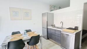 A modern kitchen with a dining table, chairs, a refrigerator, a sink, and a countertop with a cutting board. - Playitas Salema Apartment (Las Playitas)