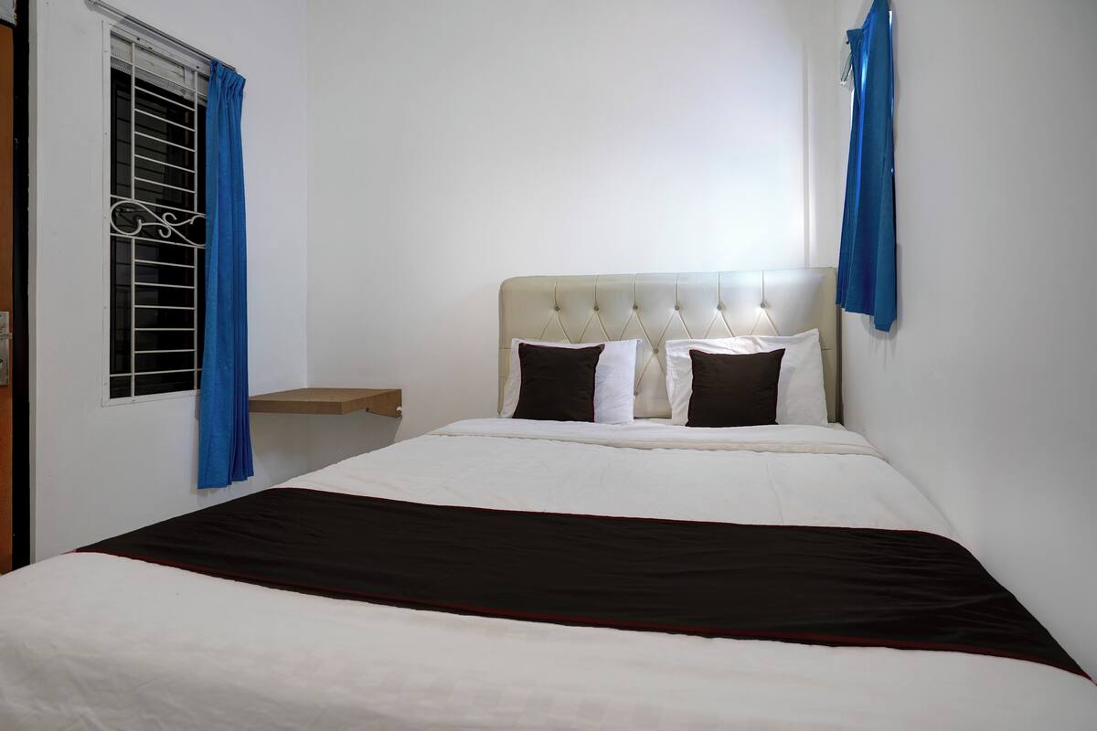 A neatly made bed with a headboard, a bedside table, and a window with curtains.