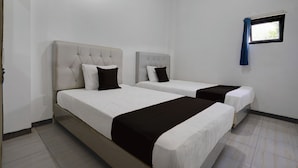 A hotel room with two beds, white bedding, and a small window with a blue curtain. - Hotel O 94843 Syariah Hj. Lilis Sukabumi (Sukabumi)
