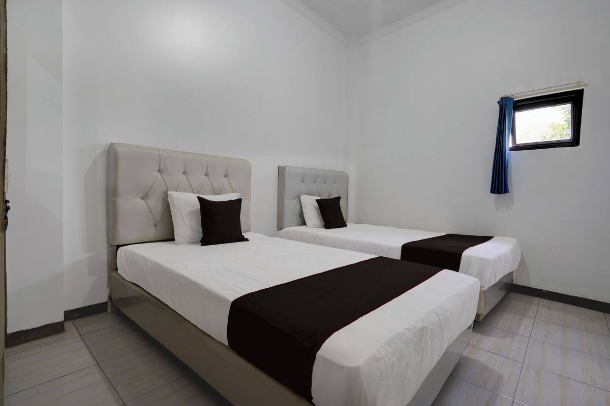 A hotel room with two beds, white bedding, and a small window with a blue curtain.