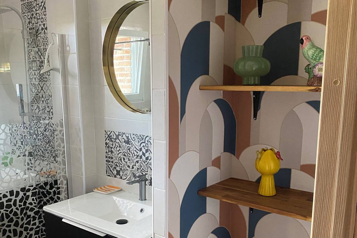 Een badkamer met een zwart-wit betegelde spatwand, een witte wastafel en een houten plank met decoratieve objecten.
