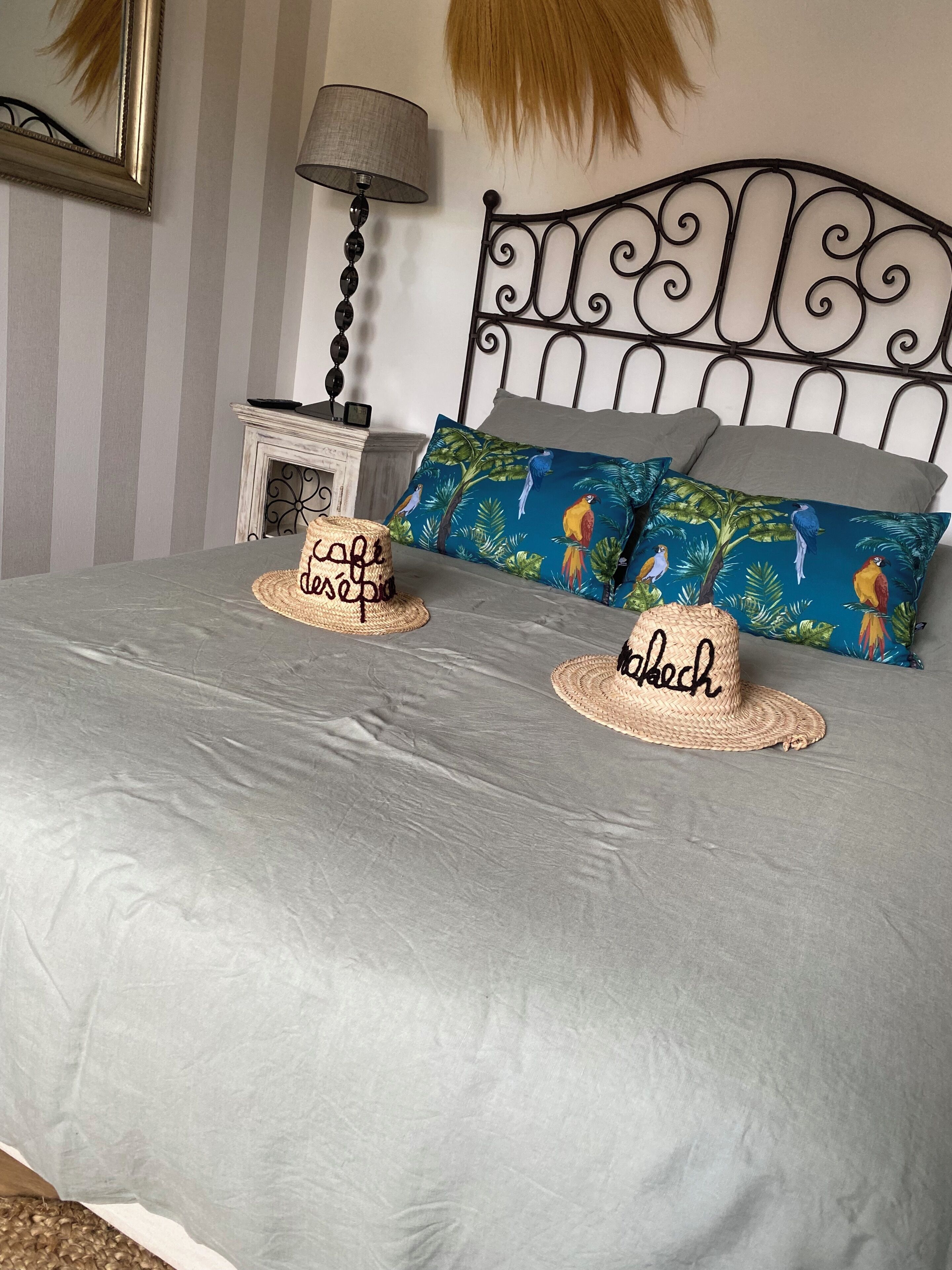 Ein ordentlich bezogenes Bett mit zwei gewobenen Hüten, einem gemusterten Kopfkissen und einer Lampe auf einem Nachttisch.