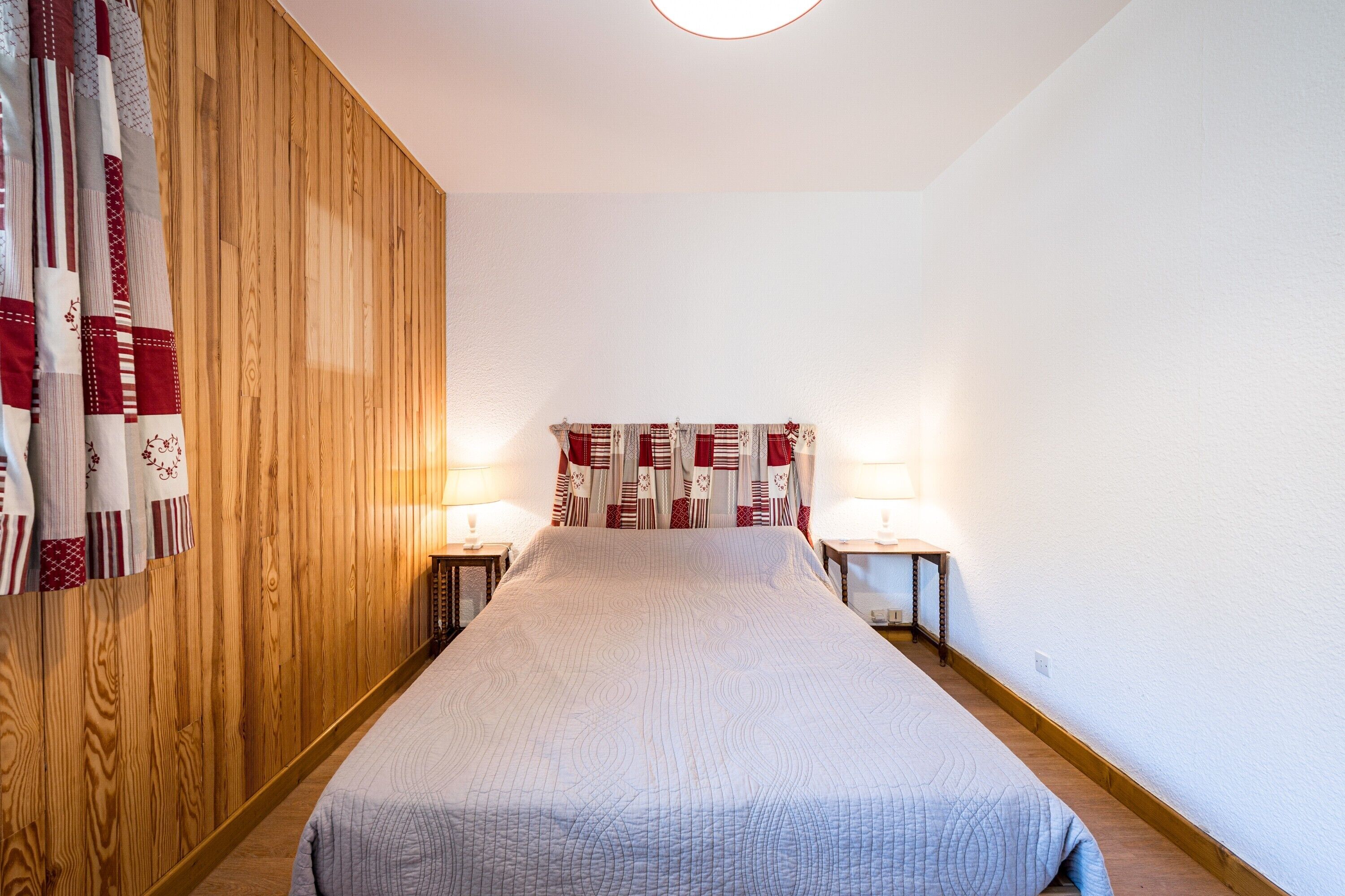 Une chambre avec un mur recouvert de panneaux de bois, un lit avec une couvre-lit matelassé, deux lampes de chevet et une tête de lit à motifs.
