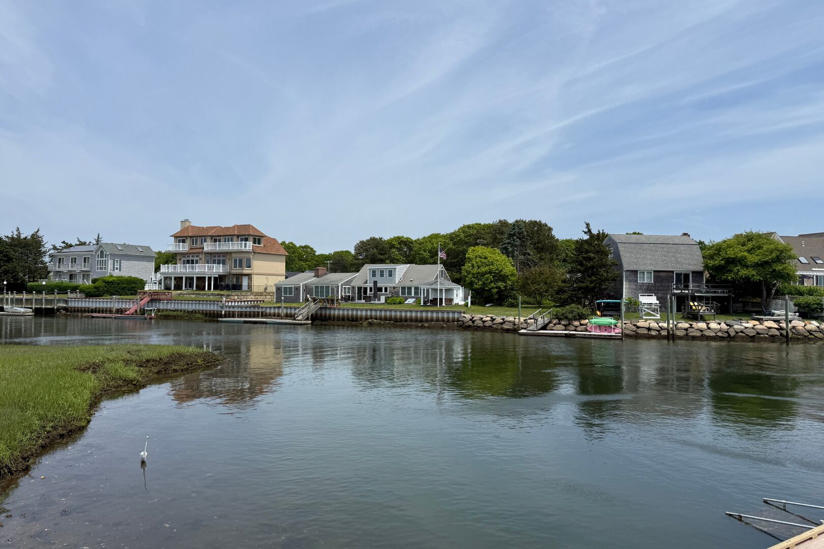 A waterfront property with a dock, a small boat, and a row of houses with a grassy area in the foreground.