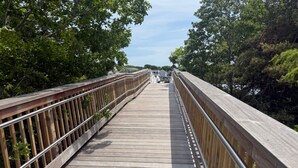 A wooden pedestrian bridge with metal railings, surrounded by trees. - Life's Better at Marshside Madness! (West Yarmouth)