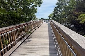 Un puente peatonal de madera con barandillas metálicas, rodeado de árboles.