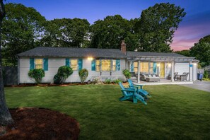 A single-story house with a covered patio, a lawn, and a tree in the foreground. - Life's Better at Marshside Madness! (West Yarmouth)