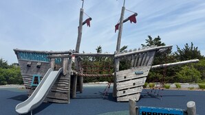 A playground with a slide, climbing net, and a ship-themed play structure. - Life's Better at Marshside Madness! (West Yarmouth)