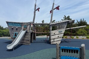 A playground with a slide, climbing net, and a ship-themed play structure. - Life's Better at Marshside Madness! (West Yarmouth)