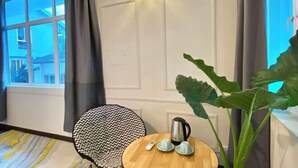A room with a large window, a round wooden table with a kettle and cups, a patterned chair, and a large green plant. - Seahome Boutique Hotel (Tanjung Bungah)