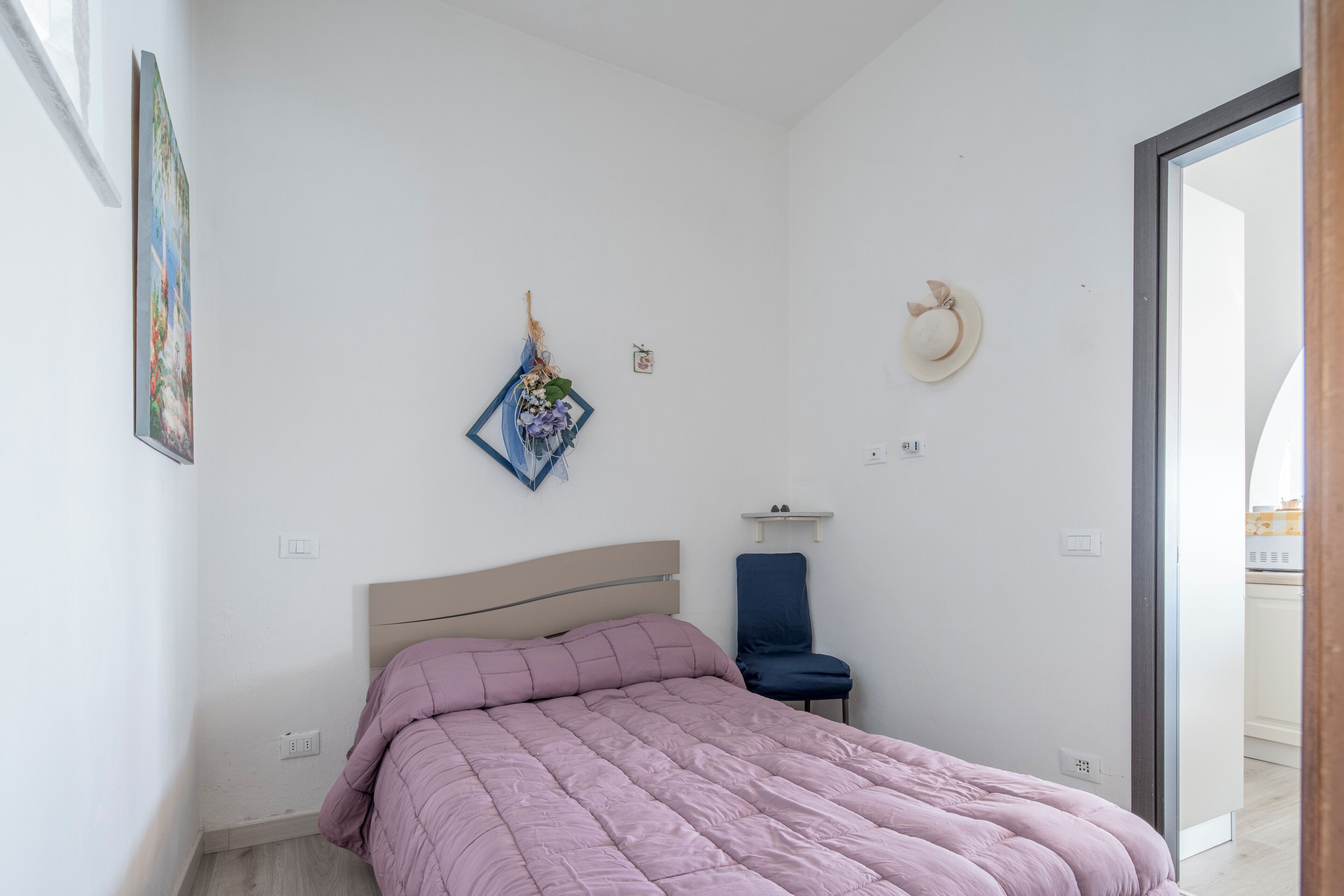 A bedroom with a bed, a chair, a wall-mounted hat, and a small shelf.
