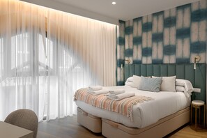Ein modernes Hotelzimmer mit einem großen Bett, einem Kopfteil mit geometrischem Muster, einem Nachttisch und leichten Vorhängen.
