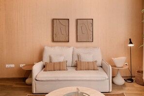 Ein stilvolles Wohnzimmer in neutralen Farben mit einer Couch, zwei Kissen, einem Beistelltisch, einer Stehlampe und zwei gerahmten Kunstwerken an der Wand.