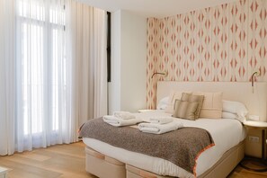 A hotel room with a bed, a nightstand, a wall-mounted lamp, and a window with sheer curtains. - Souvirón de Torres II (Málaga)