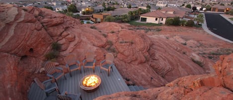 Eine Terrasse mit Adirondack-Stühlen und einem Feuerkorb mit Blick auf eine Wohngegend, Häuser und einen Berg im Hintergrund.