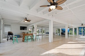 A spacious indoor area with high ceilings, multiple ceiling fans, and a large table with chairs. - Flamingo Bayou A (Fort Myers Beach)