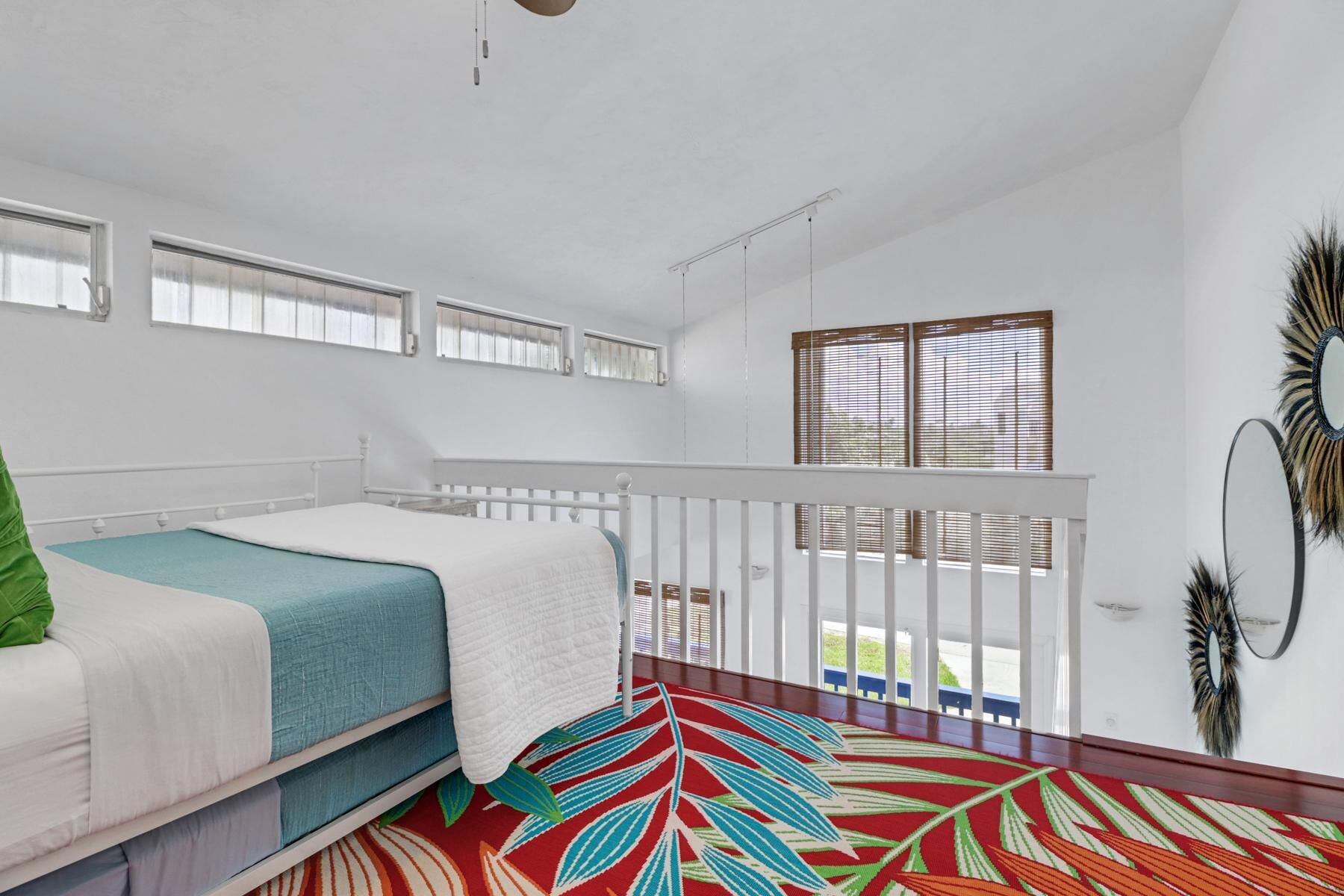 Une chambre à coucher avec un lit, un tapis coloré, un balcon avec une balustrade et une fenêtre avec des stores.