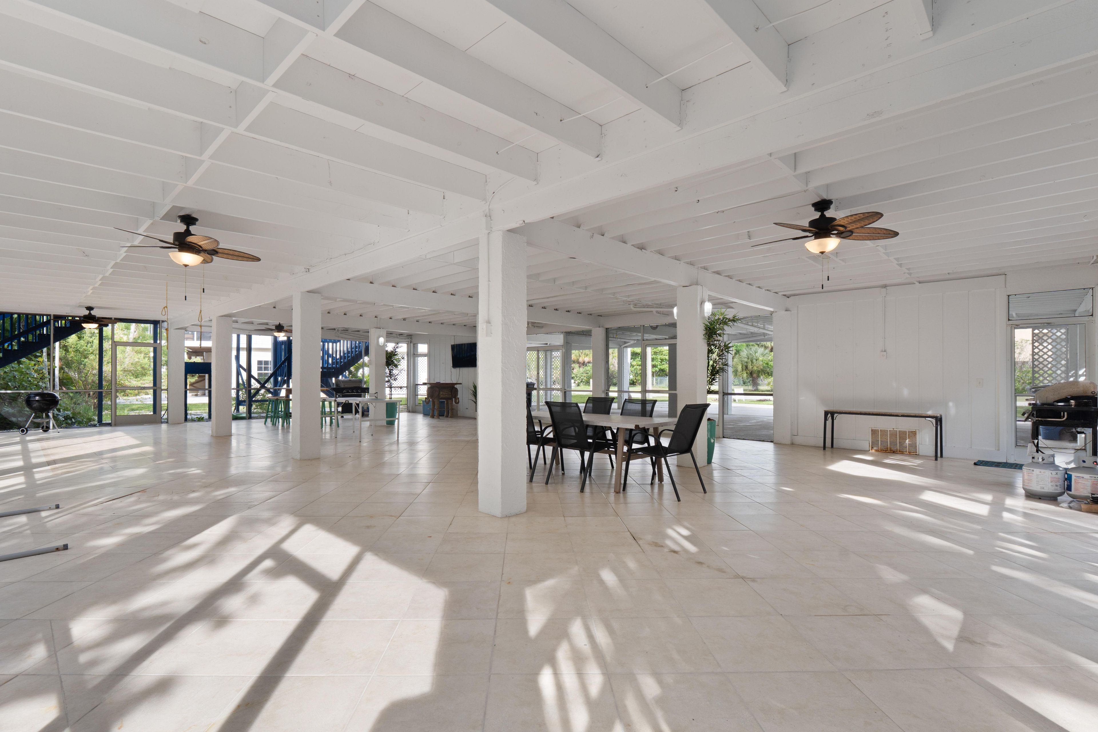 A spacious indoor area with high ceilings, large windows, and a central dining table with chairs.