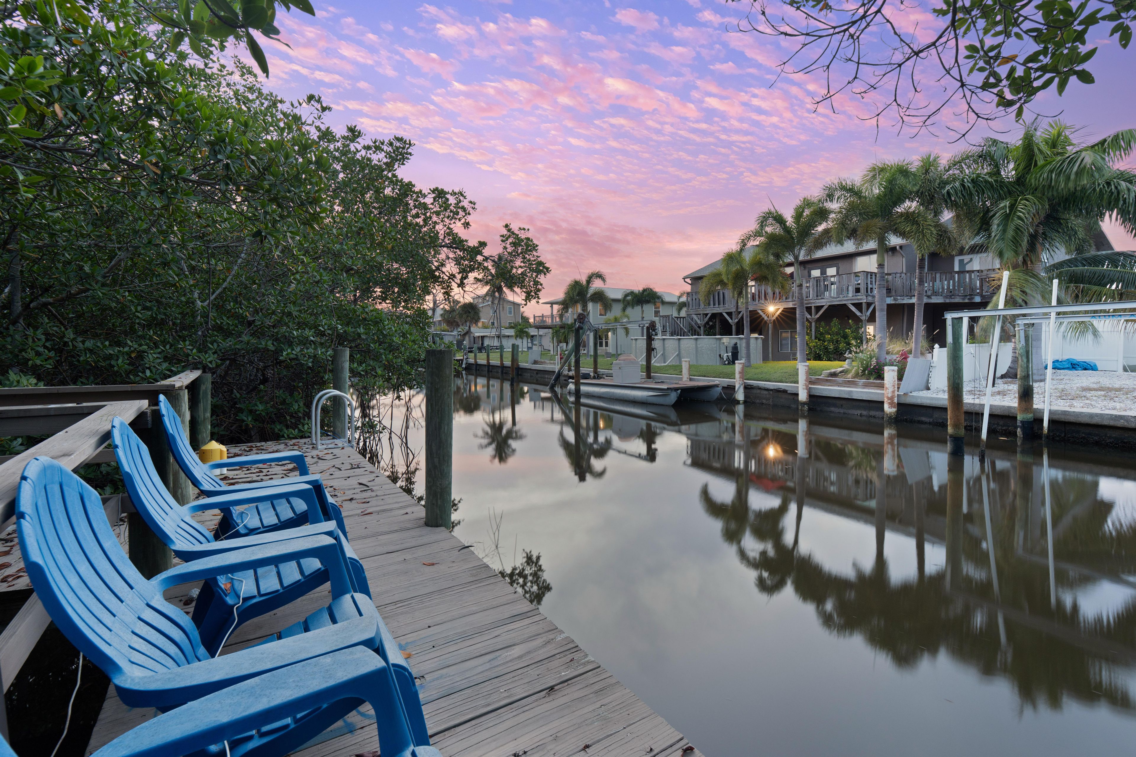 A wooden dock with blue chairs, a calm water body, and a building with a balcony in the background.