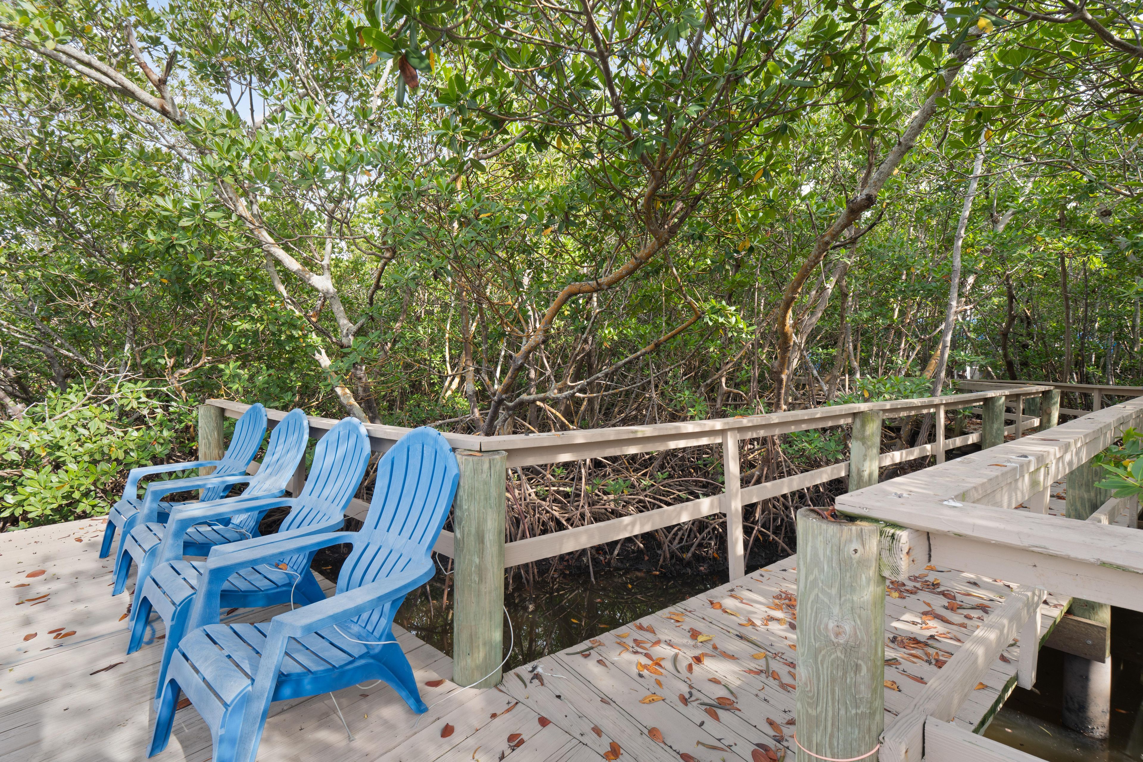 A wooden deck with blue chairs, surrounded by a wooden railing and dense foliage.