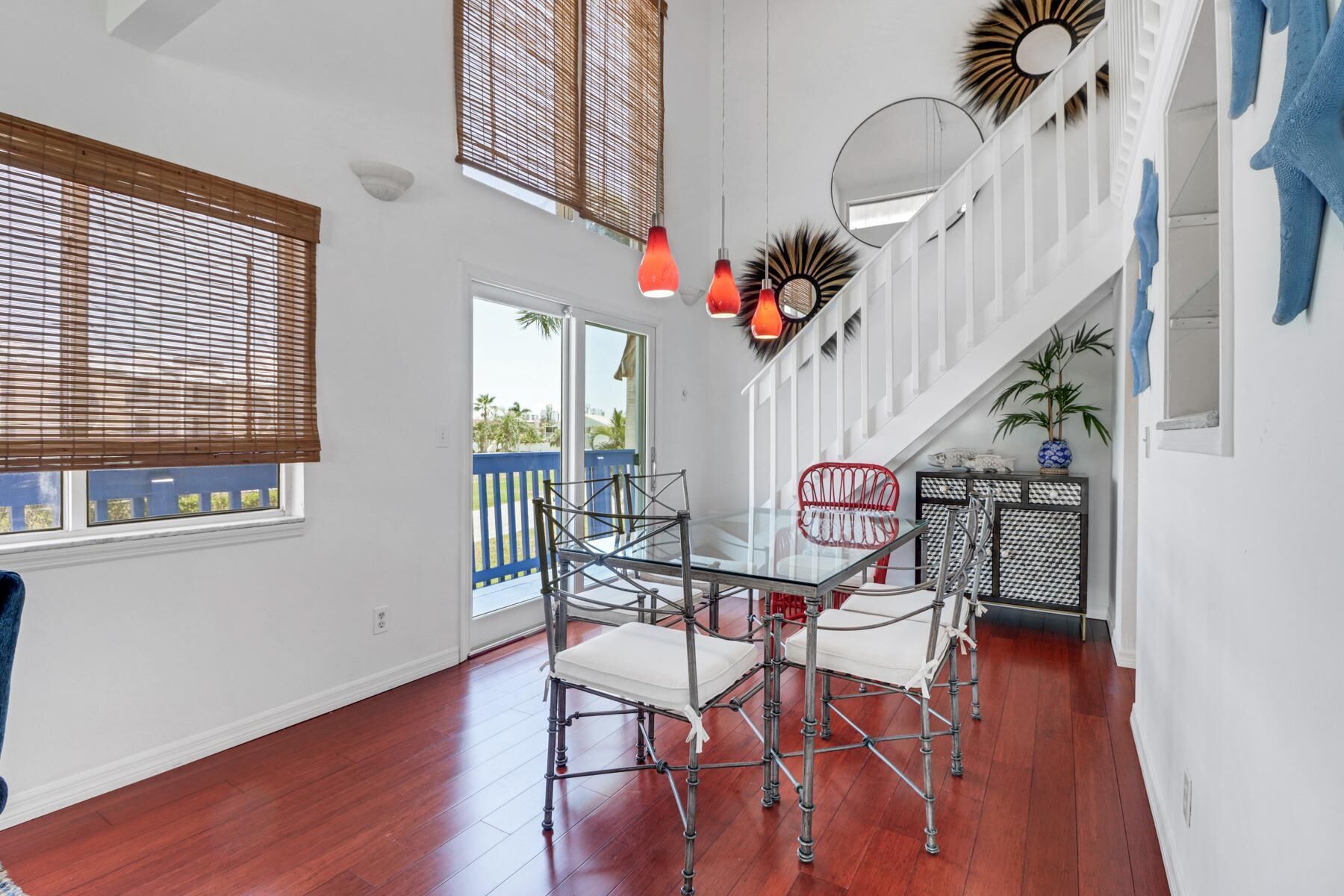 A spacious room with a glass table and chairs, wooden blinds, a staircase, and a view of the outdoors.