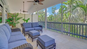 A covered outdoor seating area with wicker furniture and a view of tropical vegetation. - Flamingo Bayou A (Fort Myers Beach)