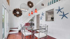 A modern dining area with a glass table surrounded by metal chairs, white walls with star decorations, and a staircase with white railings. - Flamingo Bayou A (Fort Myers Beach)