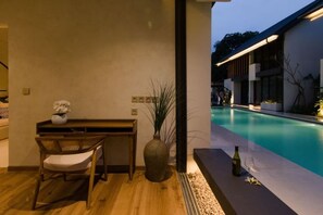 A modern indoor pool area with a wooden table and chair, a vase with flowers, and a bottle on the poolside. - Umahan Sanur (Bali)